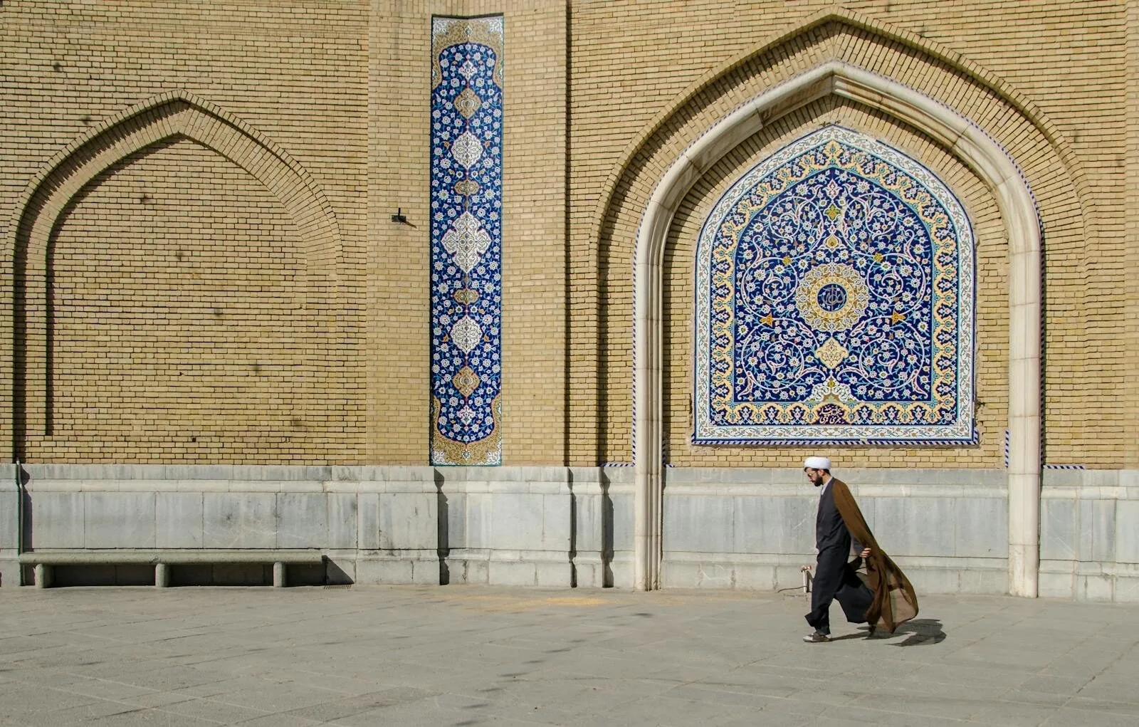 Middle-Eastern man walking past a beautifully decorated mosque wall in Qom, Iran.